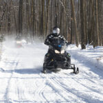 A snowmobiler coming into a clearing from the woods