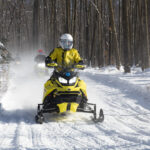 A snowmobiler leading a group coming into a clearing from the woods
