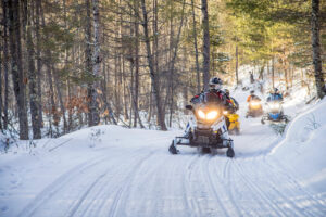 A group of people snowmobiling in a snowy wooded area
